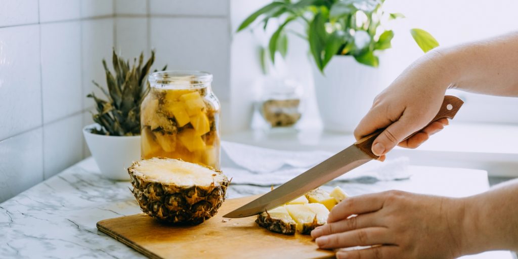A jar of Tepache with a person preparing a pineapple