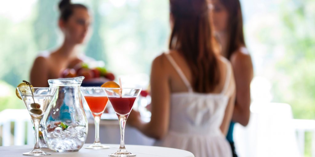 A table of cocktails with three ladies standing in a group behind it. 