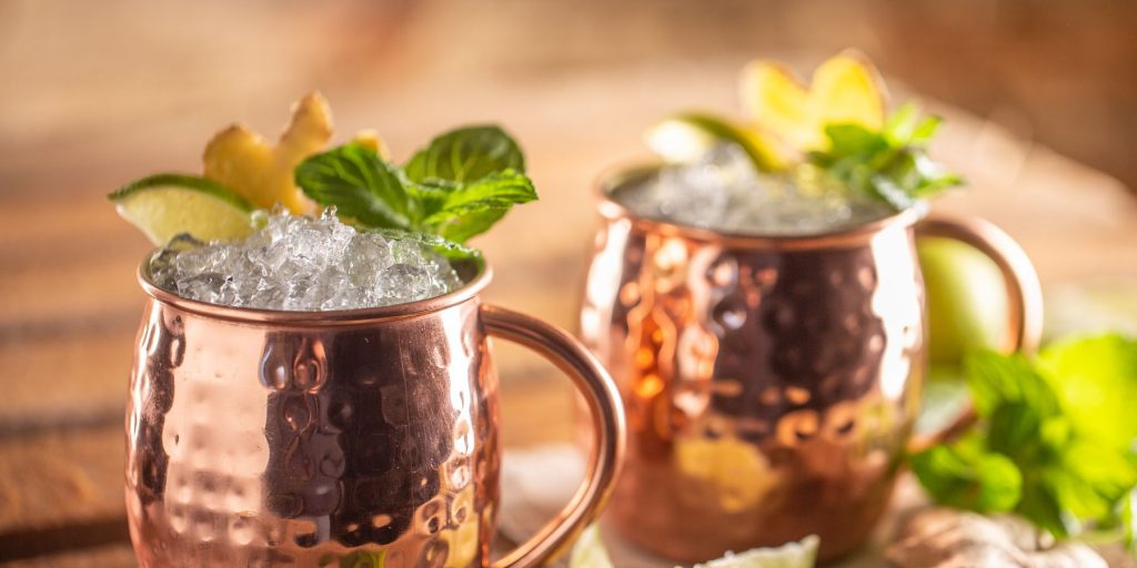 A pair of refreshing Irish Mule cocktails in copper mugs, garnished with mint and lime, set against a wooden backdrop