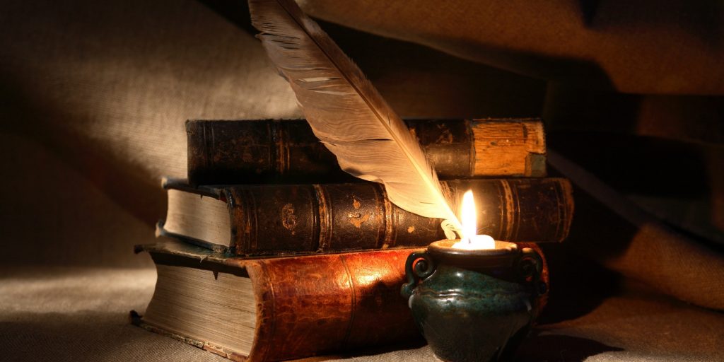 A stack of old books with a feather and a candle