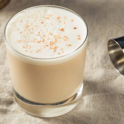 A Brandy Milk Punch cocktail in a rocks glass on a table with a cocktail jigger