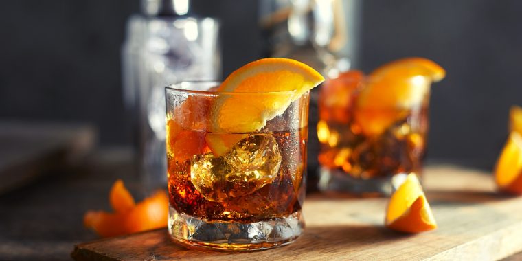 Two Irish Whiskey Old Fashioned cocktails with fresh orange garnish served on a wooden platter