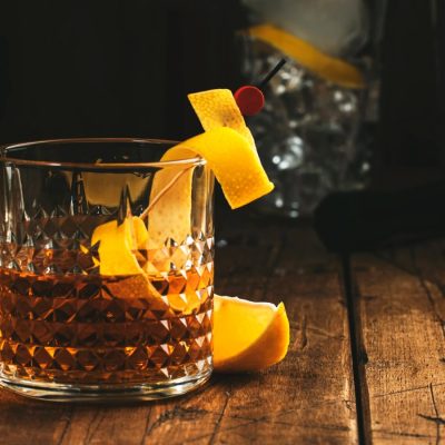 A Sazerac cocktail on a wooden table garnished with a lemon peel twist