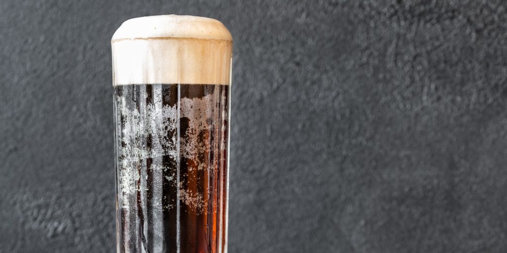 A close-up of a bougie Black Velvet cocktail with beer and Champagne in a frosted glass against a dark grey background