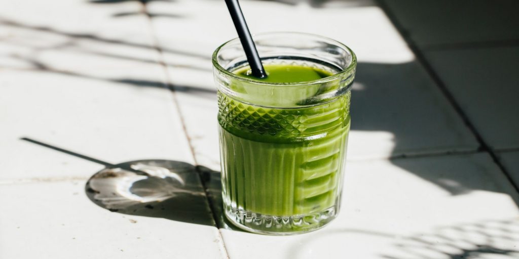 Close-up of a Green Bloody Mary cocktail with tomatillo juice as base in a retro rocks glass, on a white surface dappled with sun-splashed shadows