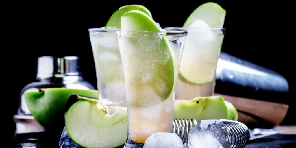 Three Bourbon & Apple Fizz cocktails garnished with fresh slices of green apple, against a dark backdrop