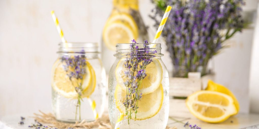 Two Lemon Lavender Gin Rickey cocktails in mason jars with a vase of lavender towards the righthand side