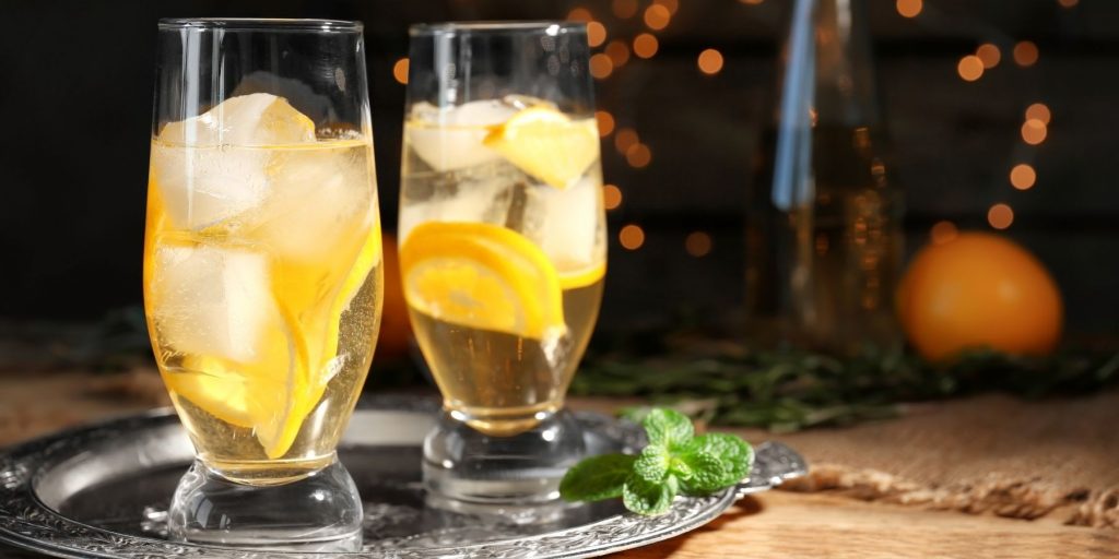 Two tall Orange Ginger Mint Sodas cocktails garnished with fresh lemon, and served on a silver platter against a dark backdrop