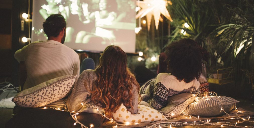 Friends enjoying an Oscar viewing party at home in an outdoor cinema setting with fairy lights and other decorations