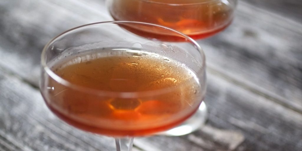 Close-up top view of two Love & Murder cocktails in coupe glasses on a grey surface 