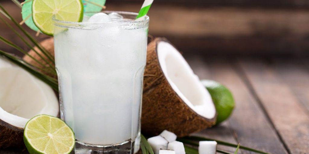 Side view of a milky Pina Verde cocktail garnished with a lime wheel, with an open coconut to the side