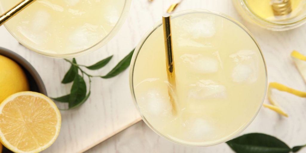 Top view of two Trato Hecho Cocktails on a white surface with green leaves around it 