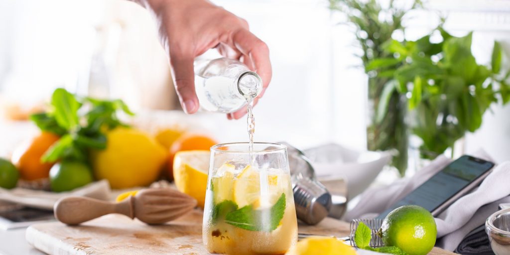 Close up side view of a home mixologist free pouring a clear liquid into a fruity cocktail