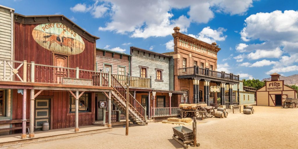 Front-side view of a Western saloon on a typical old-timey dirt road with blue skies and clouds in the background