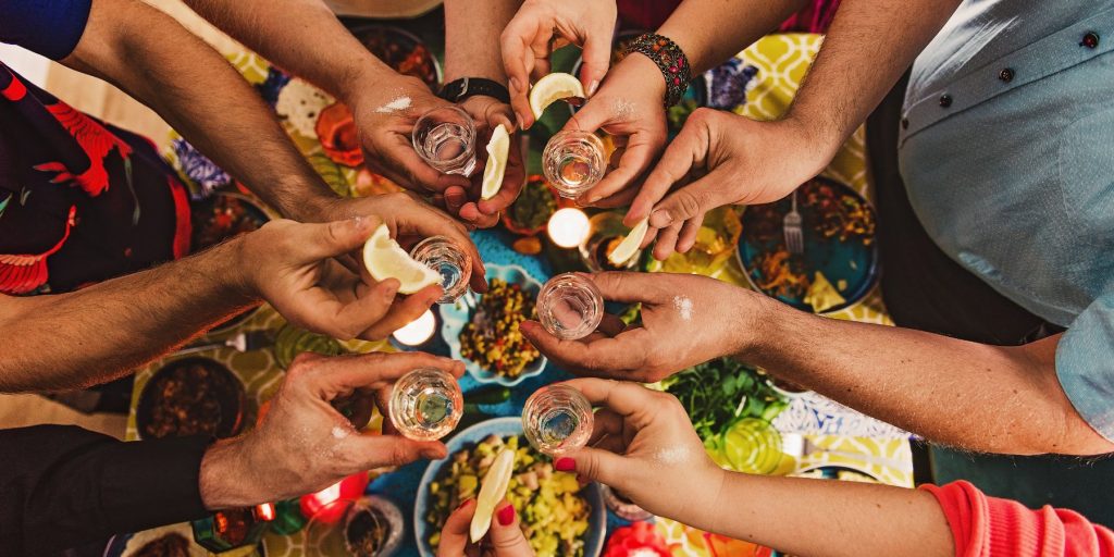 Top view of a group of friends clinking shot glasses over a table filled with Mexican food