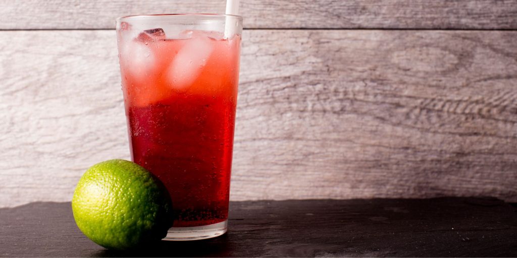 Close up of a Cherry Lime Rickey on a wooden surface with a whole fresh lime next to it