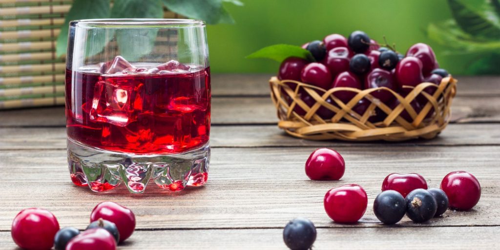 Close up of a Cherry Negroni in a rocks glass on a white wooden surface surrounded by fresh cherries