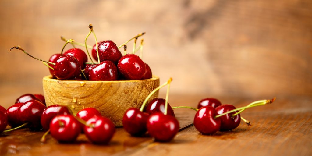 Close up of fresh cherries in a wooden bowl on a wooden surface againt a marble backdrop