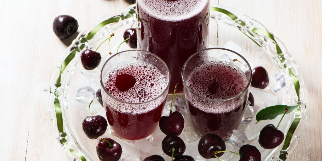 Close up top view of two Sleep Girl Cherry Juice Mocktails on a clear serving platter on a white surface surrounded by fresh cherries