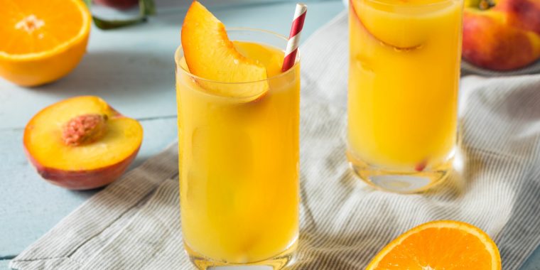 Fuzzy Navel cocktail in a highball glass with sliced peach garnish