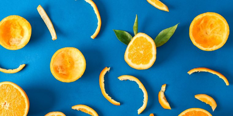 Close up top view of a collection of orange peels and slices on a bright blue backdrop