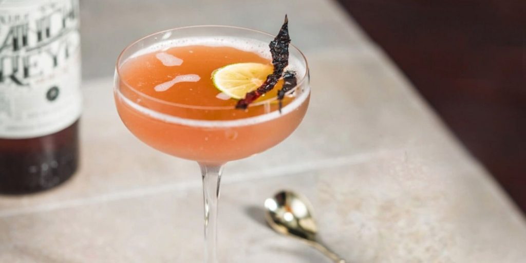 Close up of an Ancho Reyes Daiquiri garnished with a dehydrated chili slice, set on a white marble surface