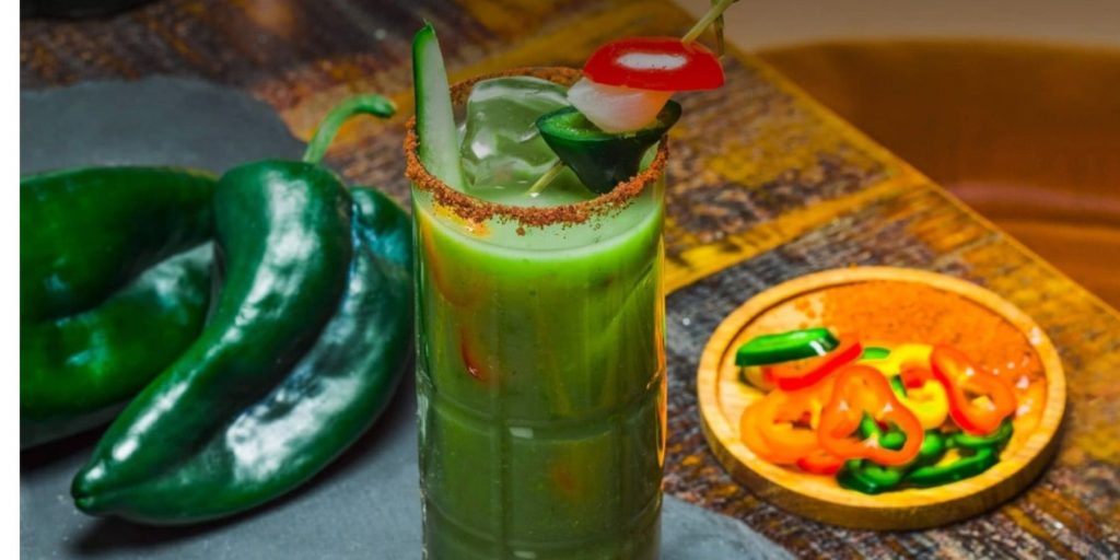 Close-up of a green and delicious Maria Verde garnished with a chilli sim and a cocktail pick with pickled onion and chili slices