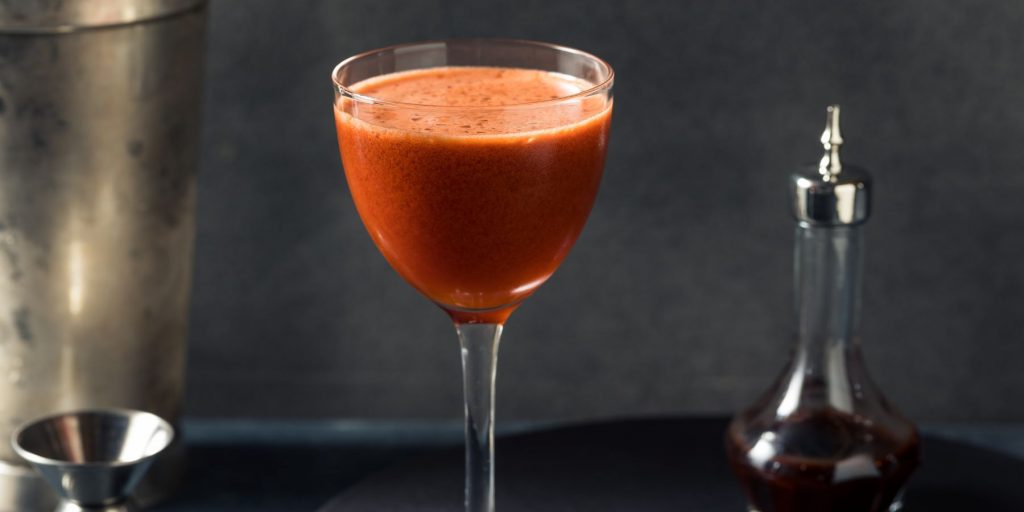 Close up of a red-hued Trininad Sour cocktail against a dark grey backdrop