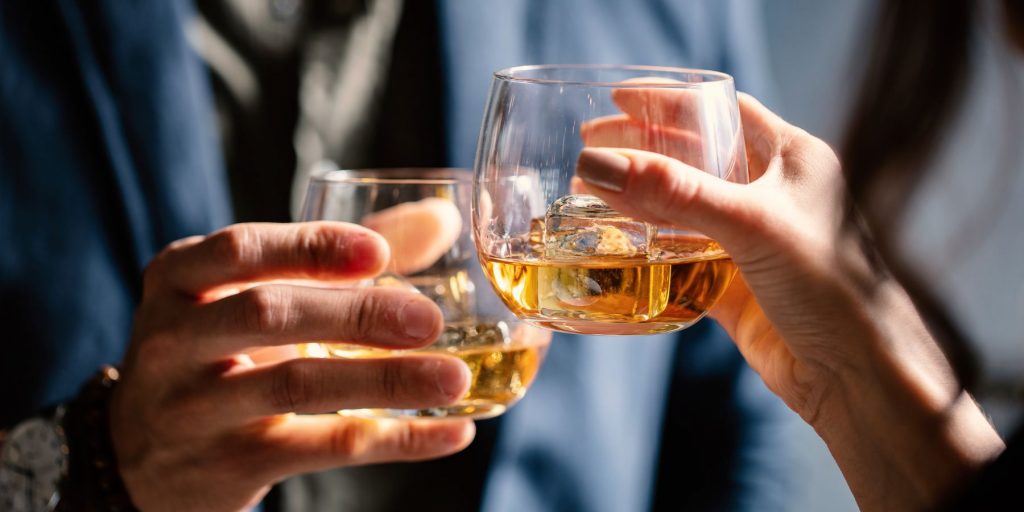 Close up of a couple clinking glasses of whiskey with clear ice cubes