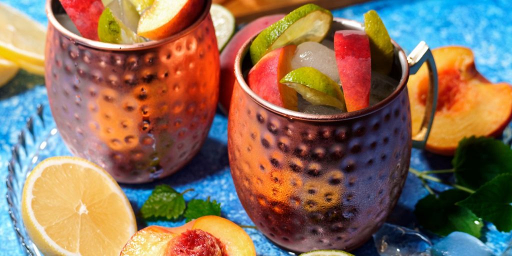 Close up of two Peach Mules in copper mugs in a bright blue surface