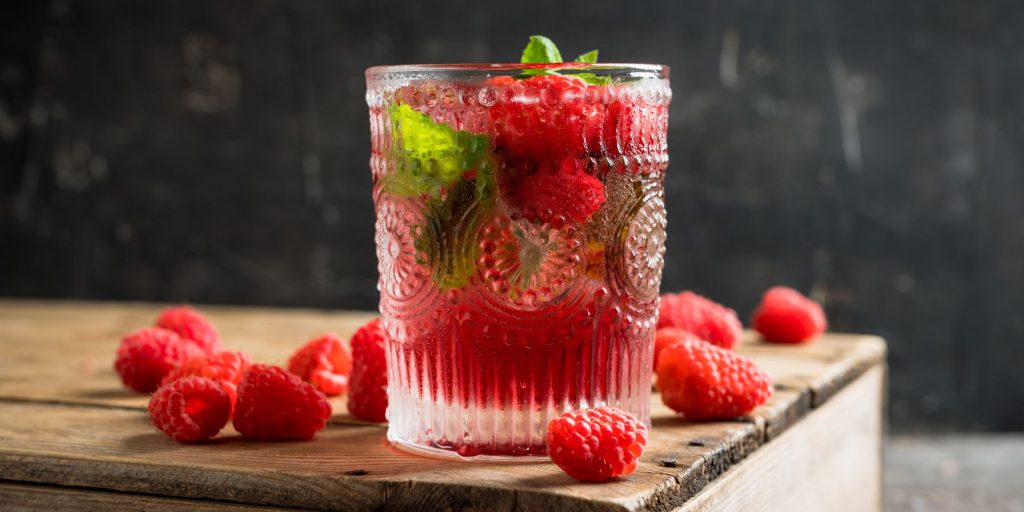  Close up of a pretty Floradora cocktail in a rocks glass on a wooden serving platter with scattered berries around it