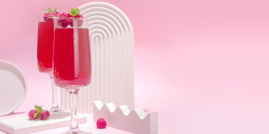 Close up front view of two Raspberry Mimosa cocktails in a stylised studio environment with a pink 