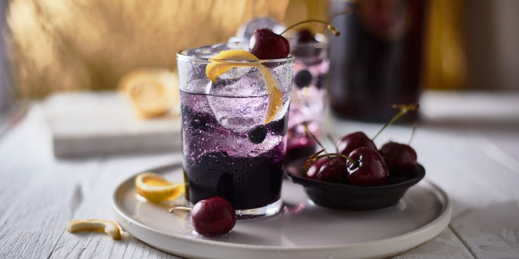 Moody shot of a pair of American Collins cocktails with blueberries and cherries
