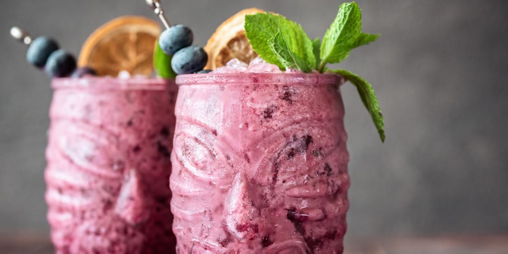 Close up of two Blueberry Colada cocktails in tiki glasses