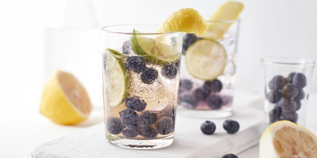Close up of a pair of Blueberry Gin Fizz cocktails against a sunny, white backdrop