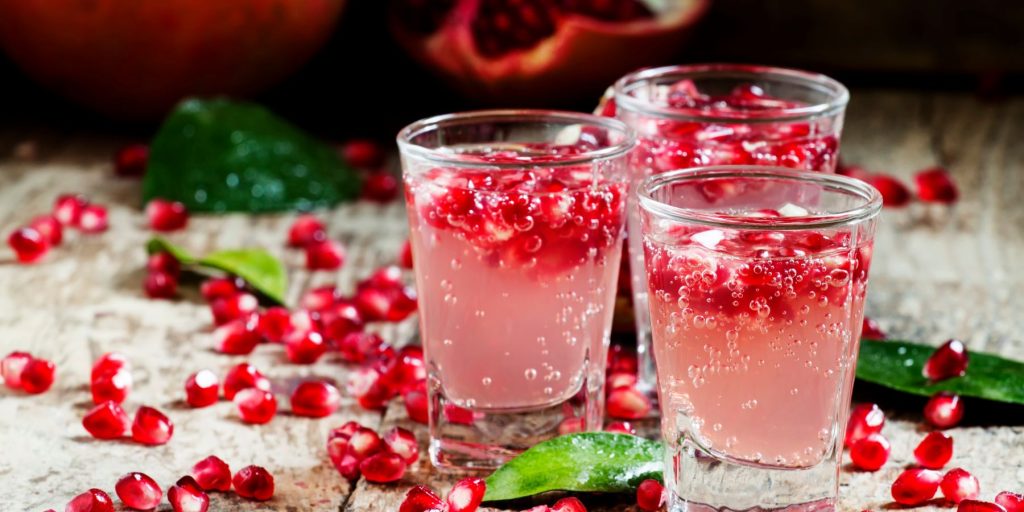 Close up of a trio of Pomegranate Gin Fizz Cocktails surrounded by pomegranate arils