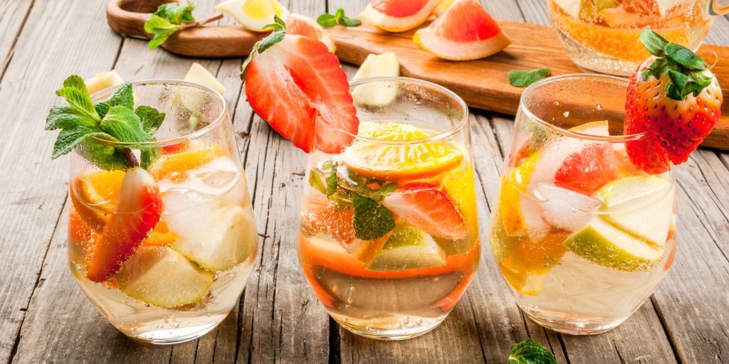 Close up of a trio of traditional White Sangria cocktails garnished with fresh fruit, against a rustic white wooden backdrop