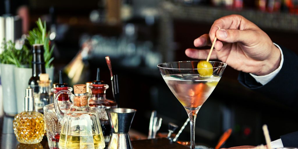 Hand garnishing a classic gin martini with an olive on a stick