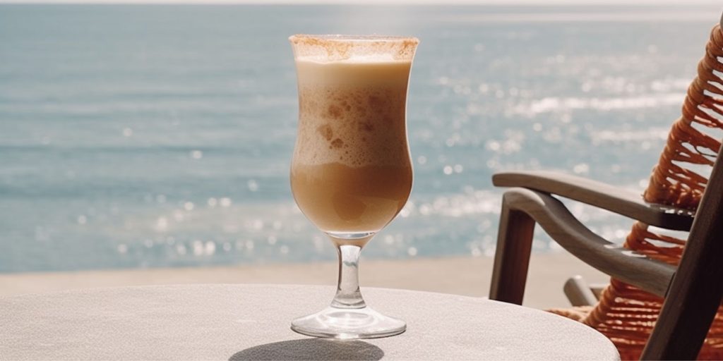 A creamy Bushwacker cocktail on a table next to a deckchar at the oceanside overlooking the sea on a sunny day 