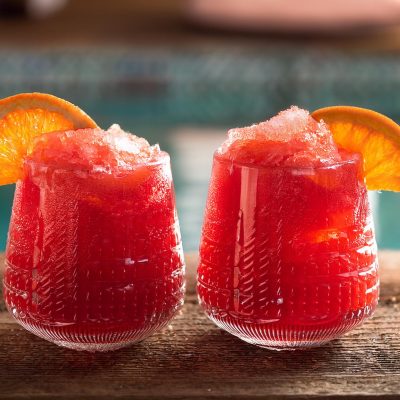 Two Frozen Negroni cocktails with orange garnish, served poolside