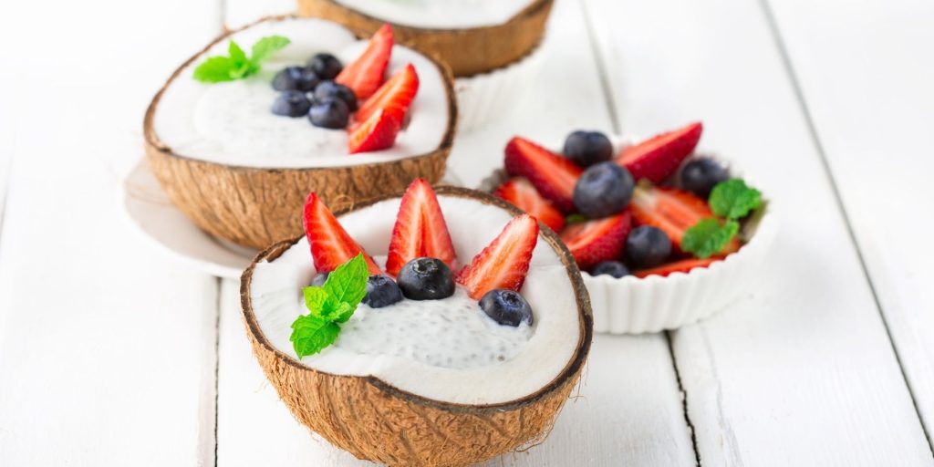 Close-up of three coconut shells filled with coconut chia pudding, garnished with berries