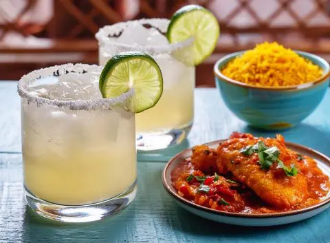 Two Tropical Spiced Rum Margaritas next to some bowls of summery snacks on a blue table in a home entertainment space