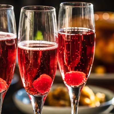 Three Kir Royale cocktails in flute glasses with raspberry garnish