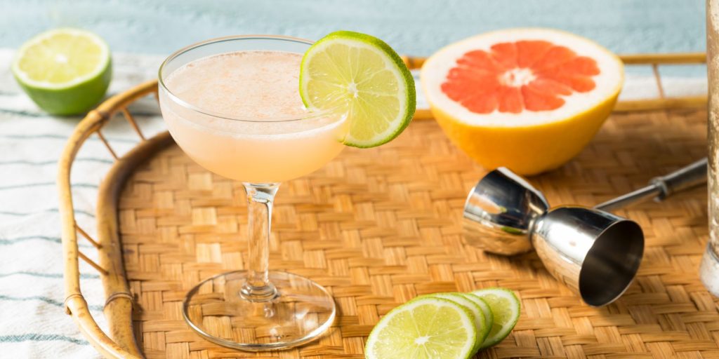 Close up of a refreshing Hemingway Daiquiri presented on a rattan serving platter along with some fresh fruit 
