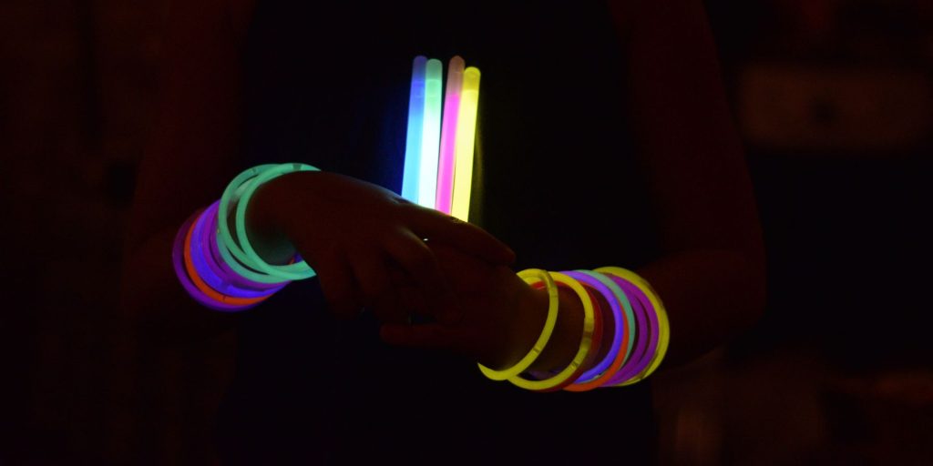 Close up of a person wearing neon arm bands holding a bunch of glow sticks in a dark room