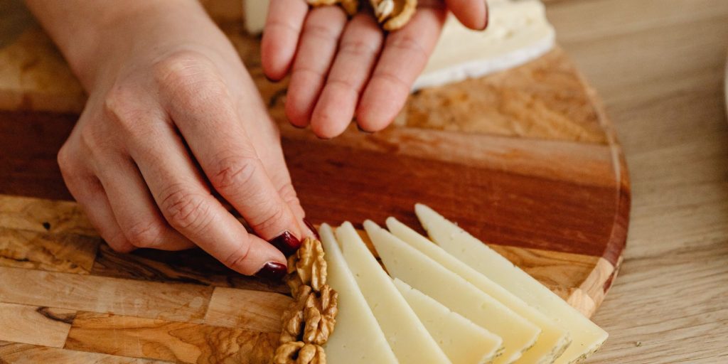 Close up of a woman's hand assembling a charcuterie platter, placing nuts and cheese in neat rows on a wooden platter