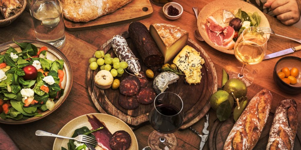 Top view of a classic charcuterie board featuring meats and cheeses, on a table surrounded by other salads, snacks and wine