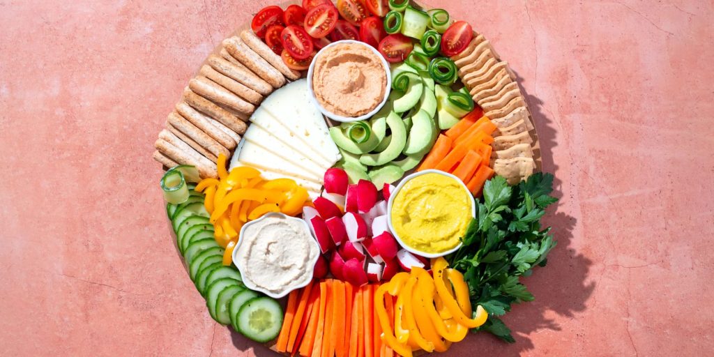 Top view of a colorful vegan grazing platter arrange on a pink surface