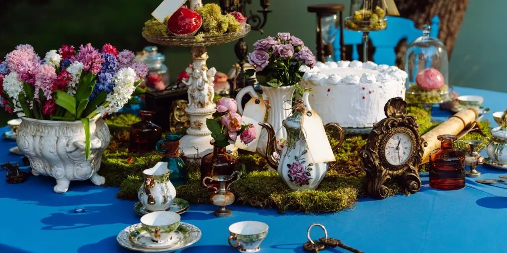 Close up of details of a table decorated for a Mad Hatter's Tea Party outside under a tree, featuring colorful flowers and various vintage-inspired decor elements