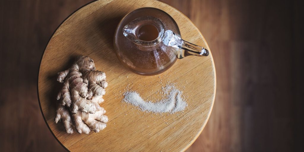 Top view of ginger simple syrup on a wooden platter along with a sprinkling of white sugar and a clutch of fresh ginger